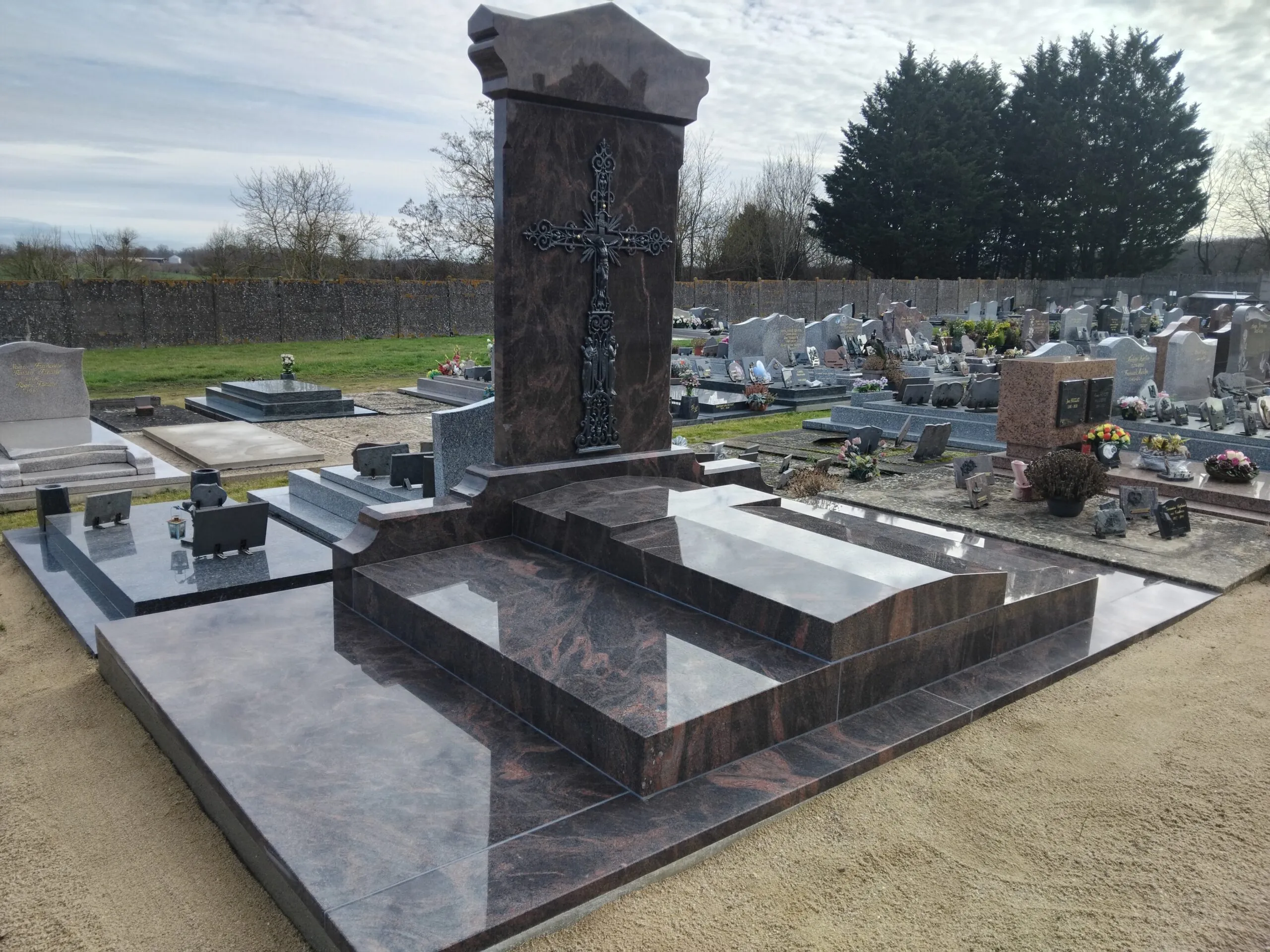 Monument funéraire imposant en granit rose et noir sculpté avec grande croix métallique