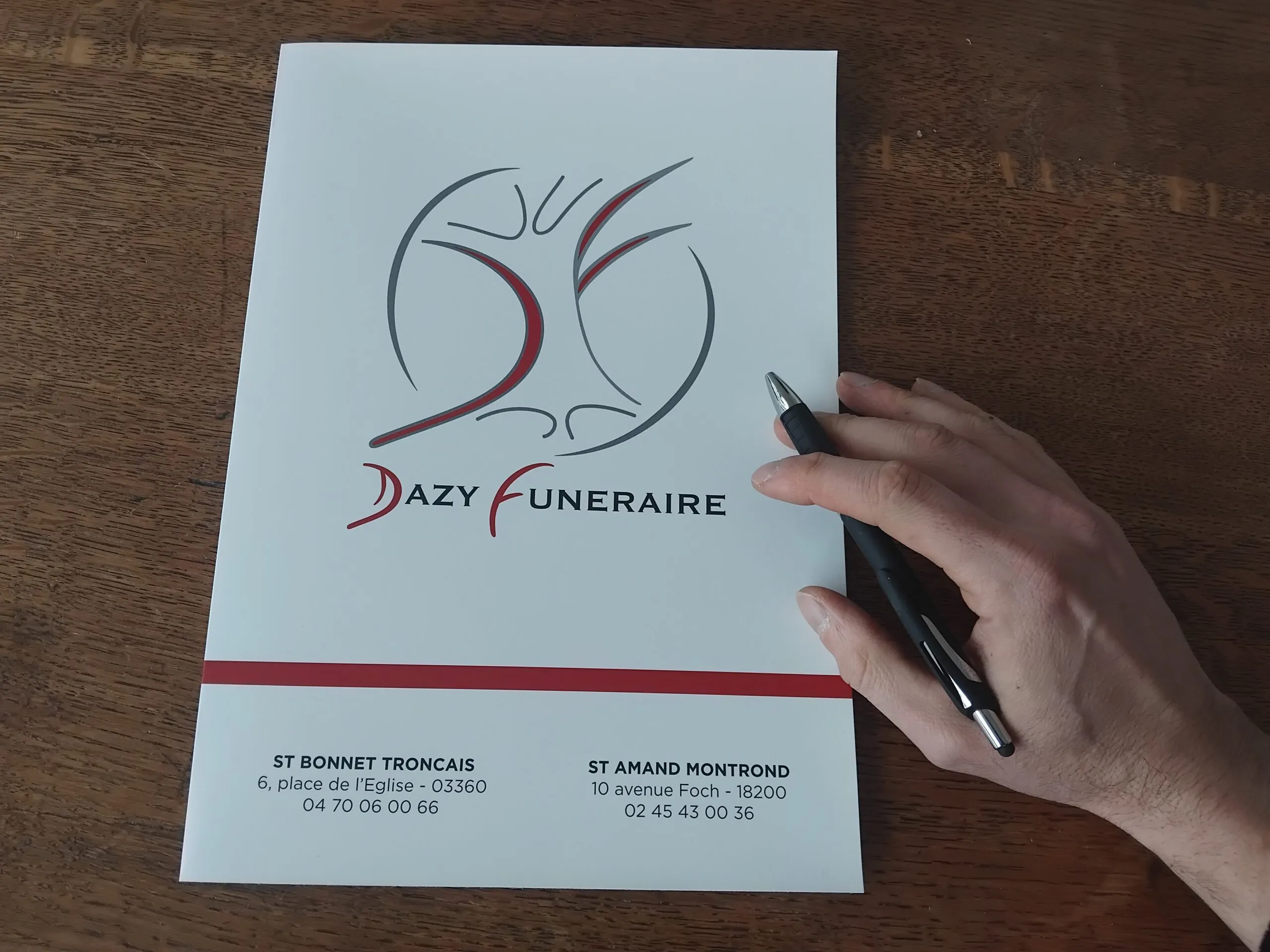 Main tenant un stylo sur une plaquette d'information de l'entreprise Dazy Funéraire