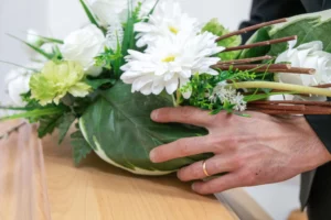 Main d'un conseiller funéraire ajustant un arrangement de fleurs blanches sur un cercueil
